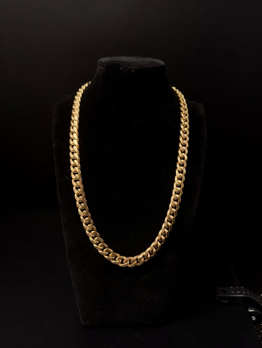 Gold chain necklace on a black velvet stand against a black background