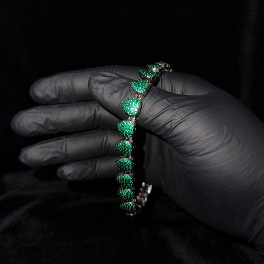 Hand wearing a black glove holding a green emerald bracelet against a dark background