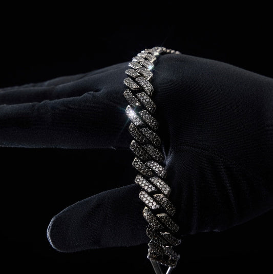 black iced out cuban link braided bracelet held by a gloved hand against a black background
