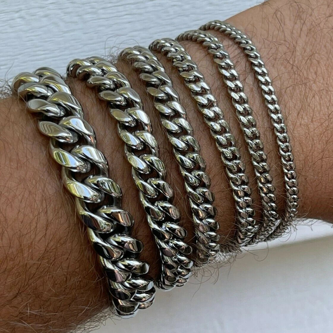 Multiple silver chain bracelets on a wrist against a white background