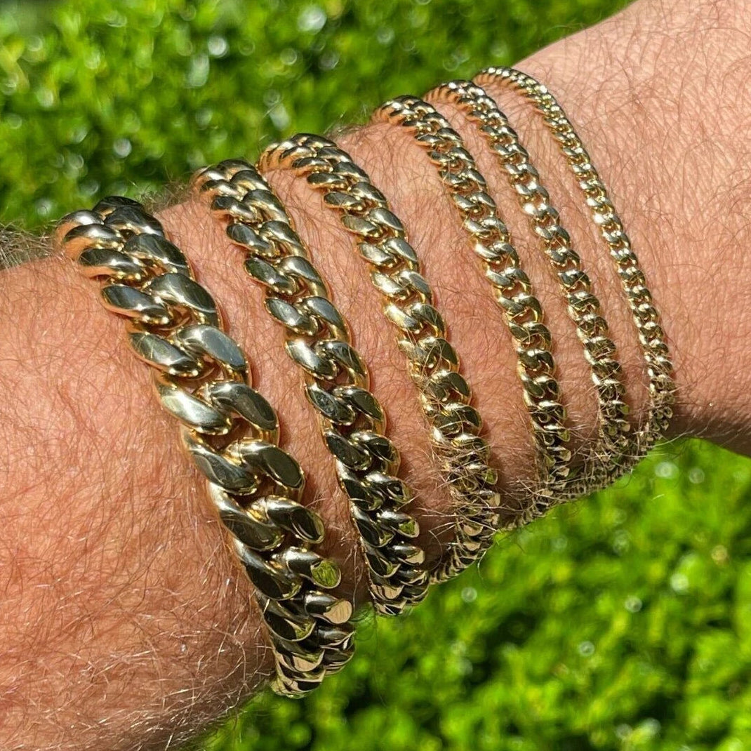Gold chain bracelets on a wrist with a green grass background